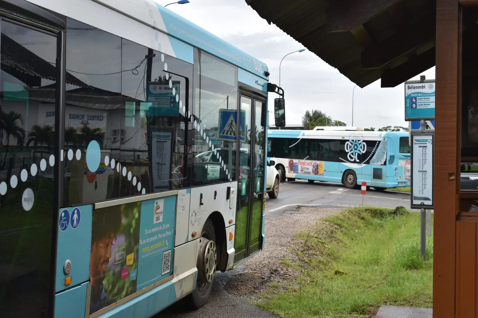 Deux bus du réseau près d’un arrêt, l’un portant un affichage publicitaire sur son flanc.